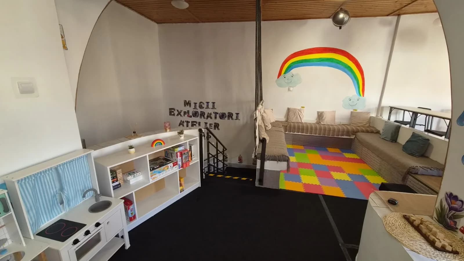 Zona Micii Exploratori Atelier, cu pictura cu curcubeu, plasă de cățărat și covor puzzle colorat