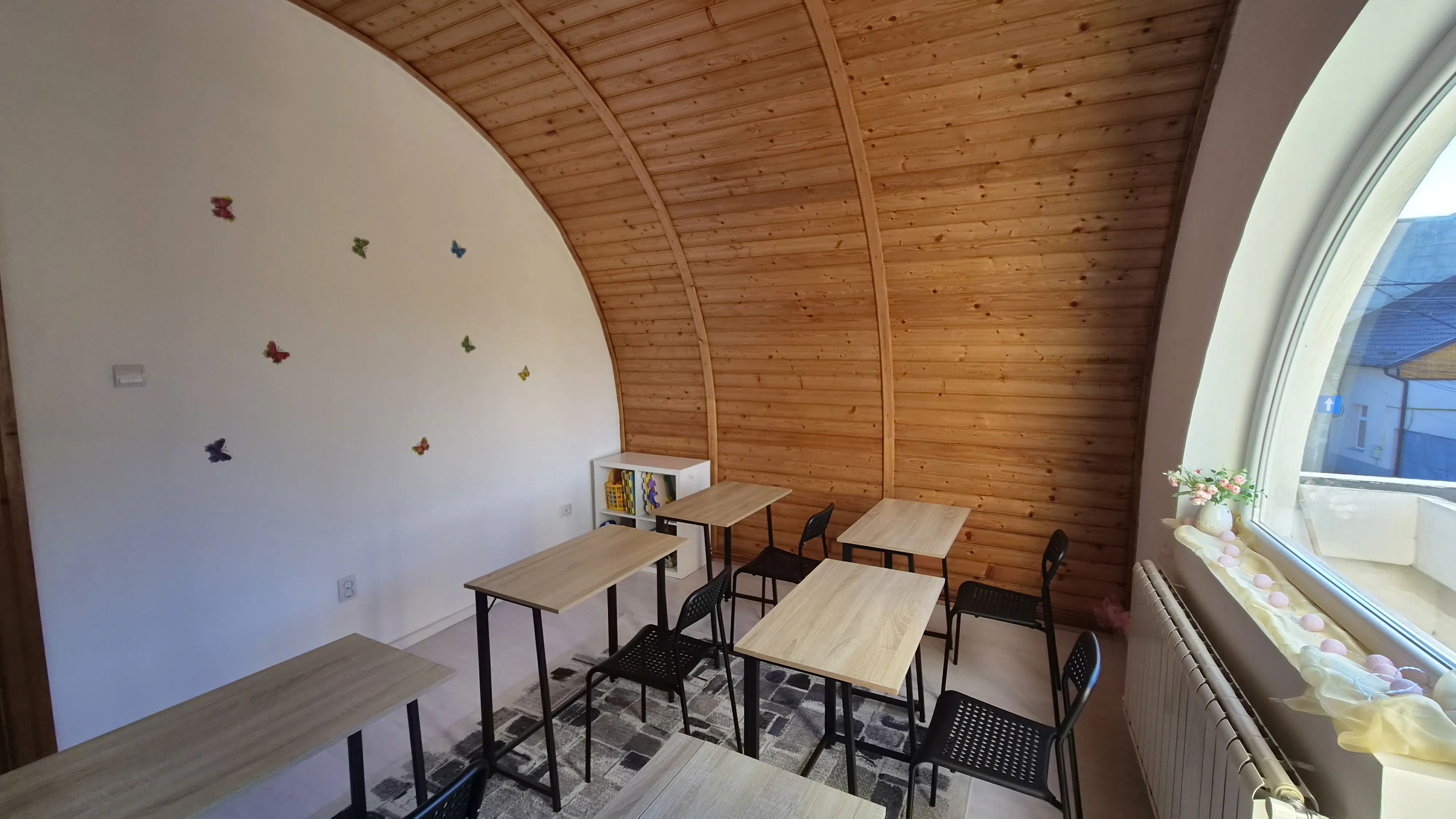 Sala de cursuri, cu autocolante de fluturi pe perete și fereastra arcuită spre stradă
