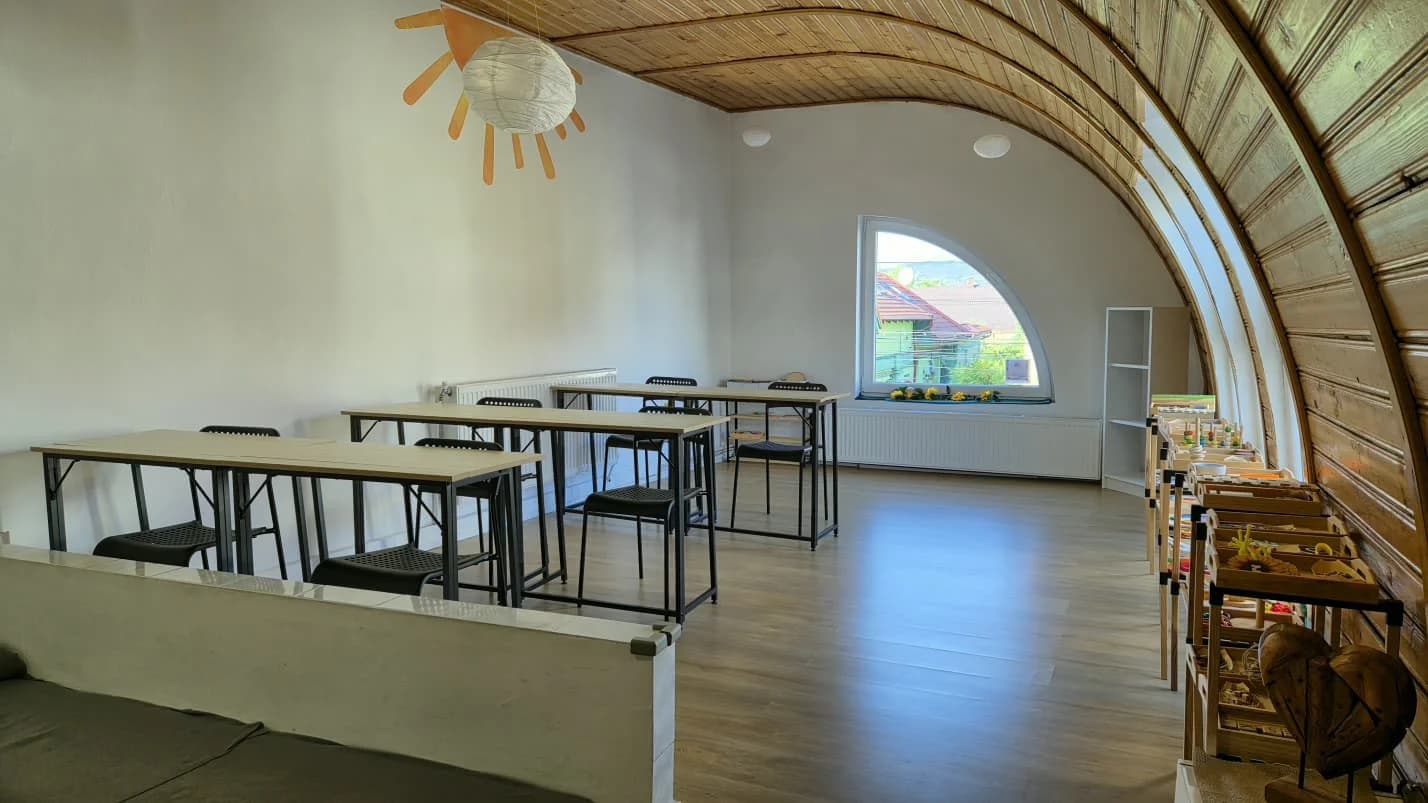 Sala de after-school PascuPas, cu tavan de lemn arcuit, mese de lucru și un soare decorativ suspendat